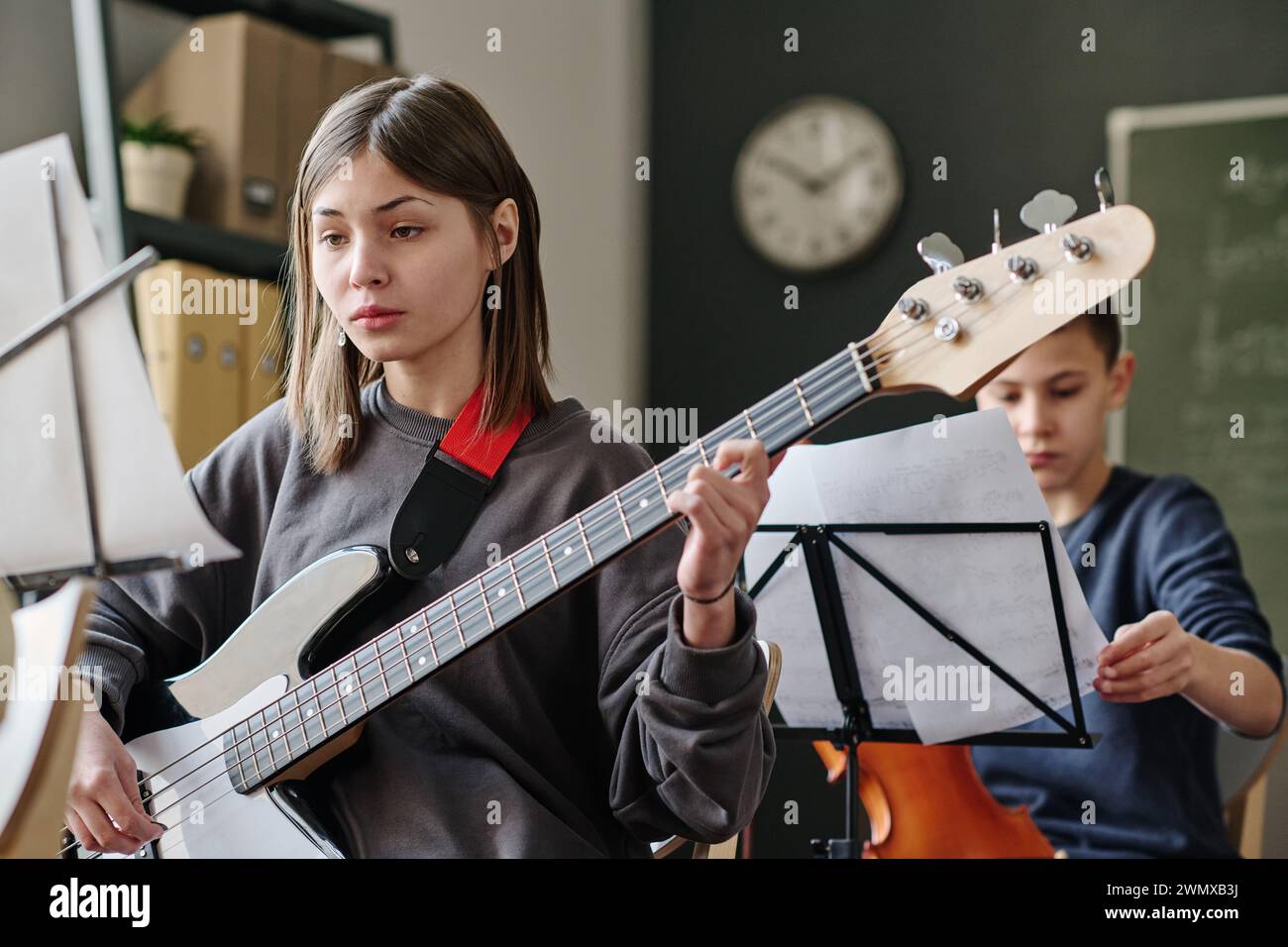 Selektive Fokusaufnahme eines kaukasischen Teenager-Mädchens, das während des Musikunterrichts in der Schule Bass-Gitarre übt Stockfoto