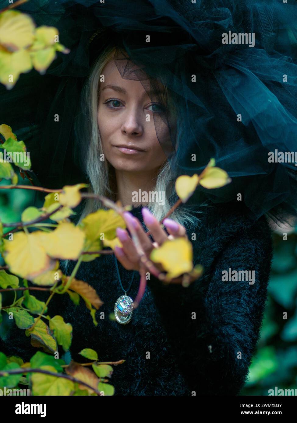 Die Frau blickt durch das Grün, ihr raffinierter Kopfschmuck schafft einen auffälligen Kontrast Stockfoto