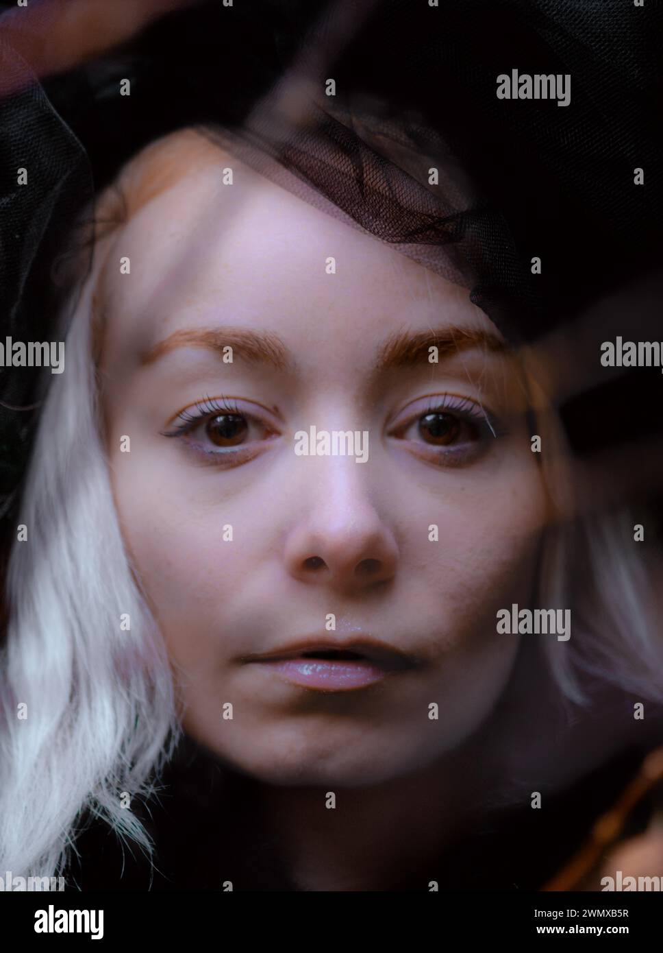 Scharfe Nahaufnahme einer weißen nordischen jungen schönen Frau Blick durch transparentes Gewebe tragen Sie schwarzen Spitzenhut Stockfoto