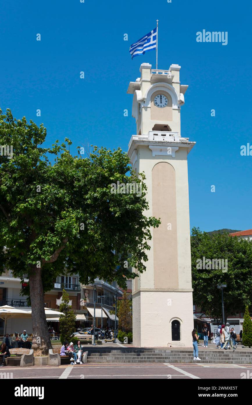 Eine Turmuhr mit der griechischen Flagge umgeben von Bäumen und Menschen in einer entspannten Atmosphäre, Xanthi, Ostmakedonien und Thrakien, Griechenland Stockfoto