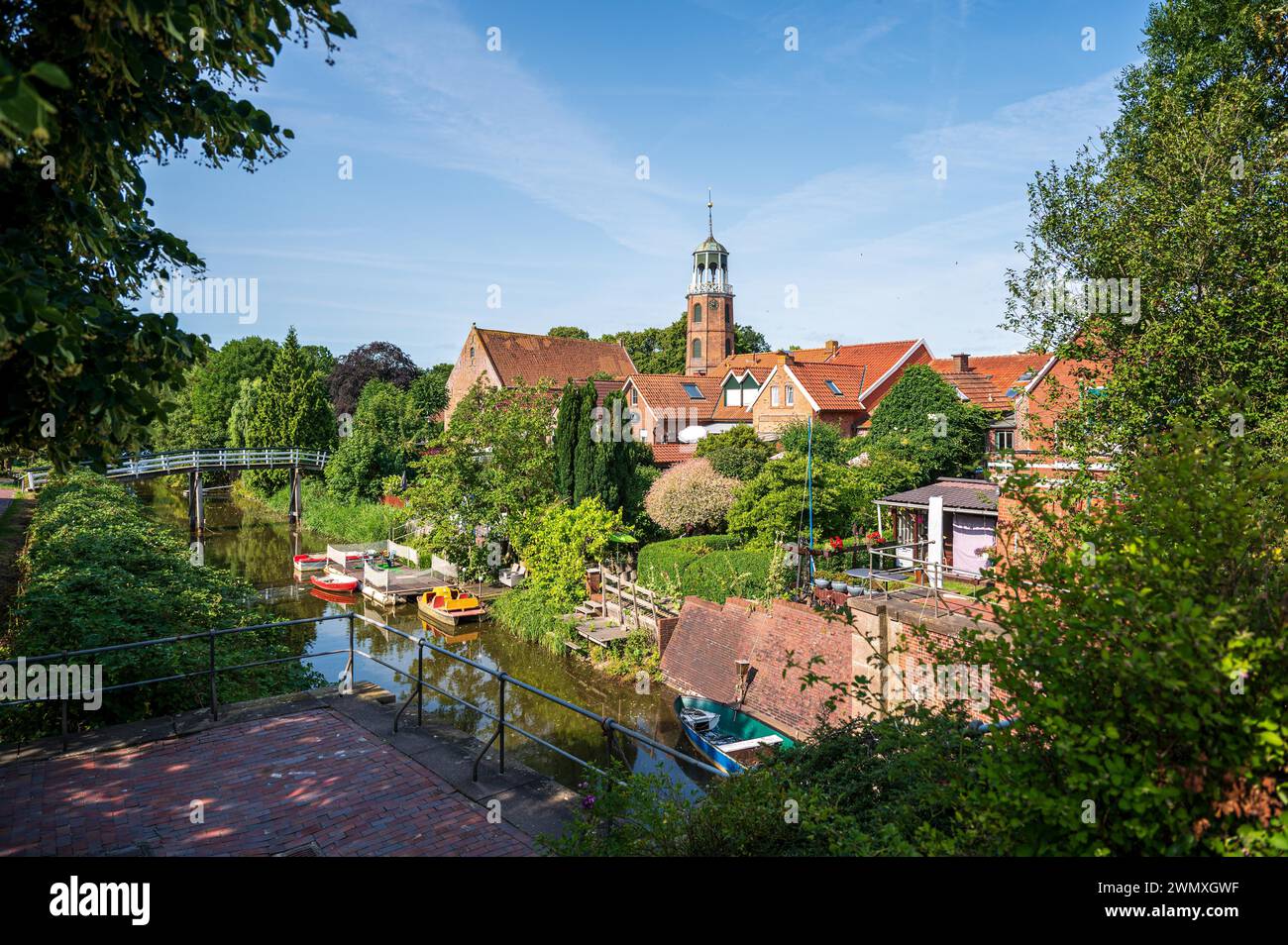 Blick auf ein malerisches Dorf mit einem Fluss, Booten und einer Kirche umgeben von üppigem Grün, Ditzum, leer, Ostfriesland, Niedersachsen Stockfoto