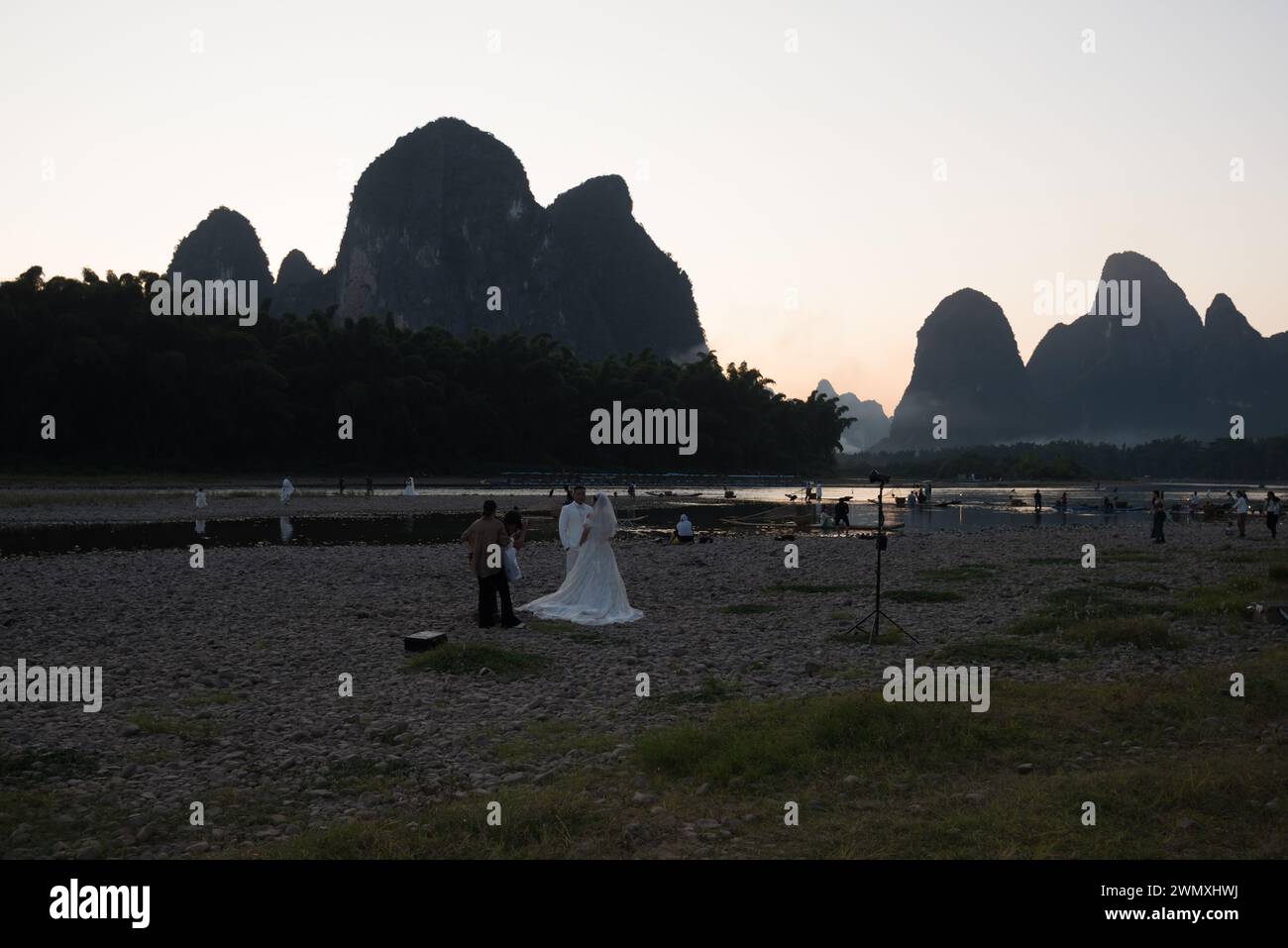 Yangshuo County, Guilin City, Guangxi, China - 23. Oktober 2023: Ein frisch vermähltes Paar macht Hochzeitsfotos am Ufer des Li-Flusses in der Abenddämmerung Stockfoto