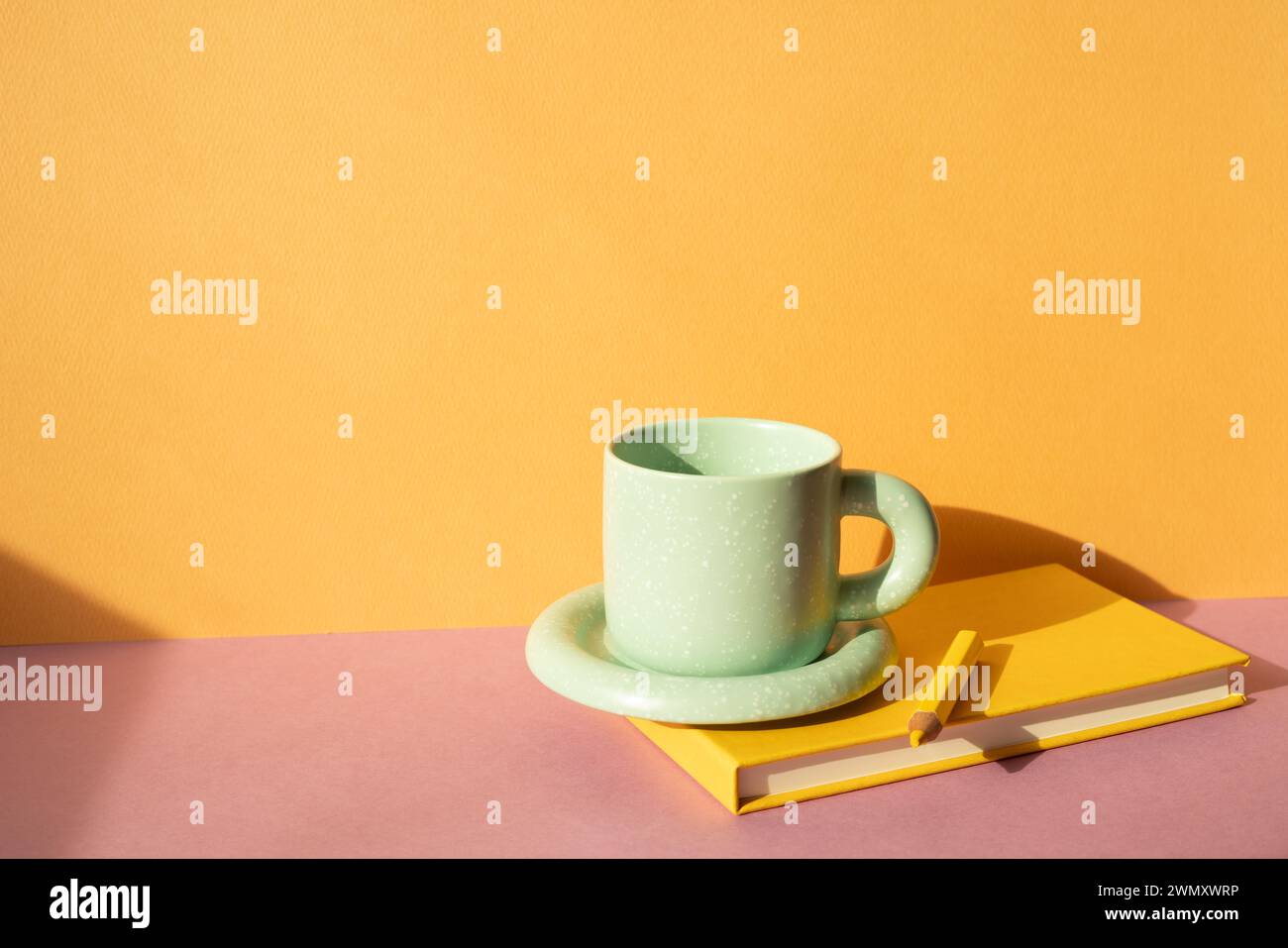 Notizbuch und Farbstift, Kaffeetasse auf rosa Schreibtisch. Orangefarbener Wandhintergrund. Arbeitsbereich Stockfoto