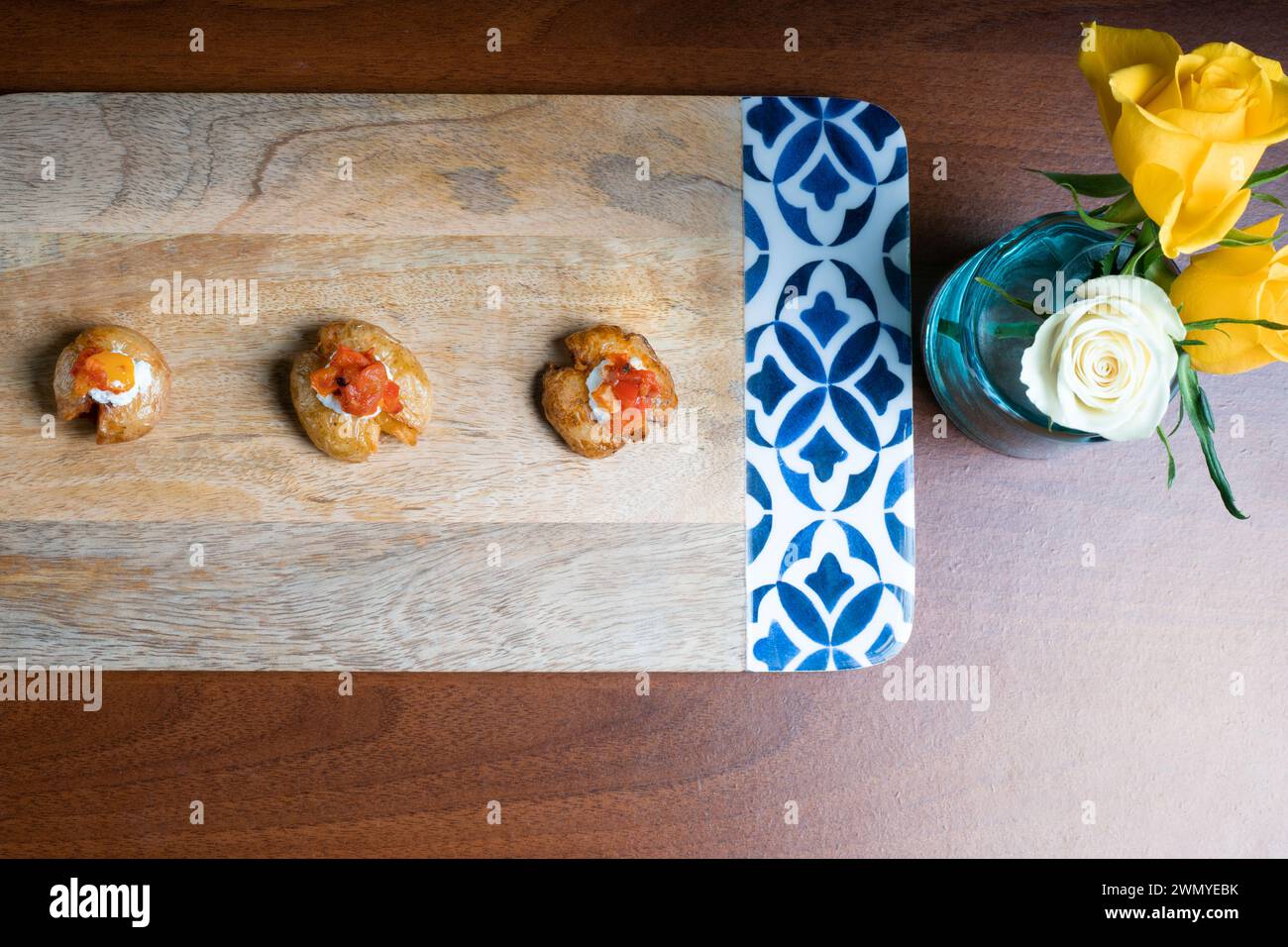 Von oben elegante Babykartoffeln mit geschmolzenem Mozzarella und rotem Pfeffer auf einer Holzplatte mit dekorativen Blumen. Stockfoto