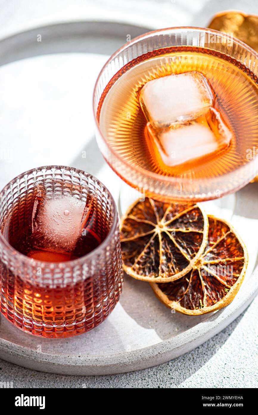 Lebhafte alkoholische Getränke werden in strukturierten Gläsern serviert, mit Eiswürfeln akzentuiert und an einem sonnigen Tag mit getrockneten Orangenscheiben garniert Stockfoto