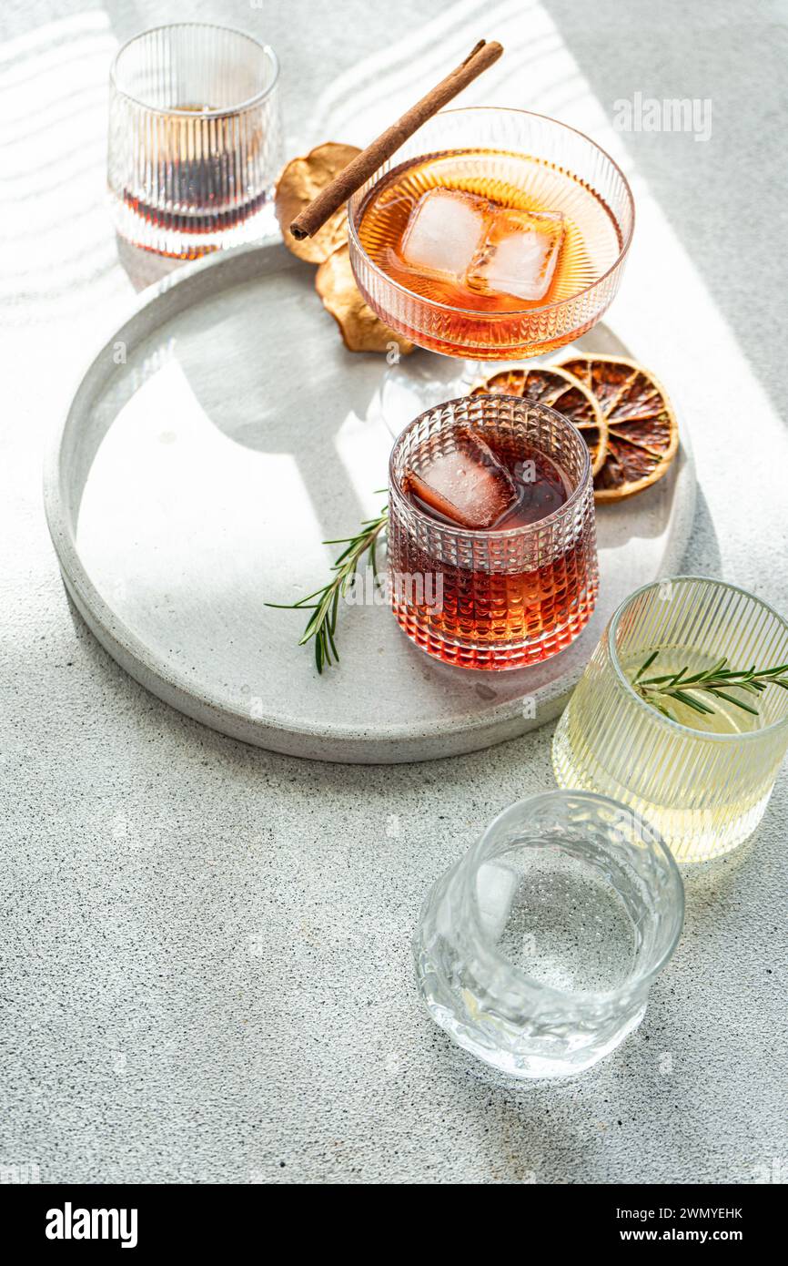 Eine Auswahl an alkoholischen Getränken in einzigartigen Gläsern, garniert mit Kräutern und Zitrusfrüchten, präsentiert auf einem runden Tablett in natürlichem Licht Stockfoto