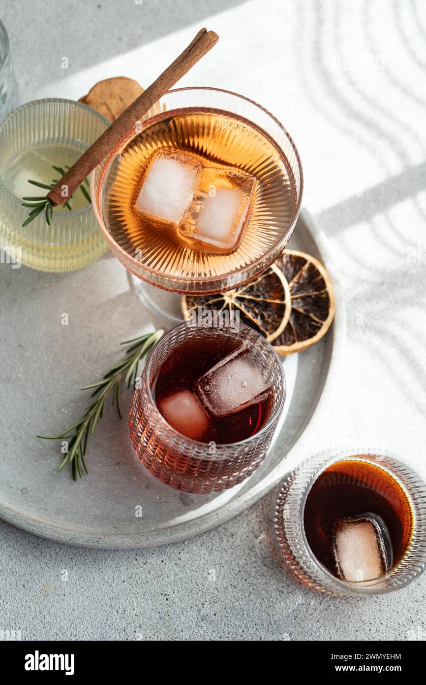 Von oben verschiedene alkoholische Getränke in strukturierten Gläsern, garniert mit Zimt, Rosmarin und getrockneten Zitrusfrüchten, auf einem runden Tablett Stockfoto