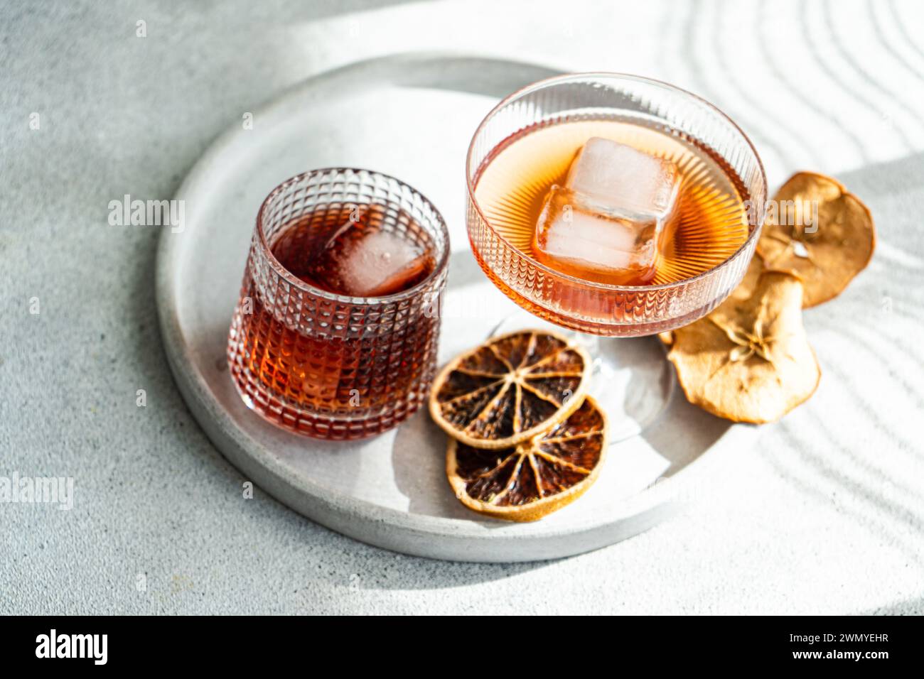 Eine gut beleuchtete, elegante Präsentation verschiedener alkoholischer Getränke in gerippten Gläsern, mit Eiswürfeln und getrockneten Zitrusfrüchten auf einem runden Tablett Stockfoto