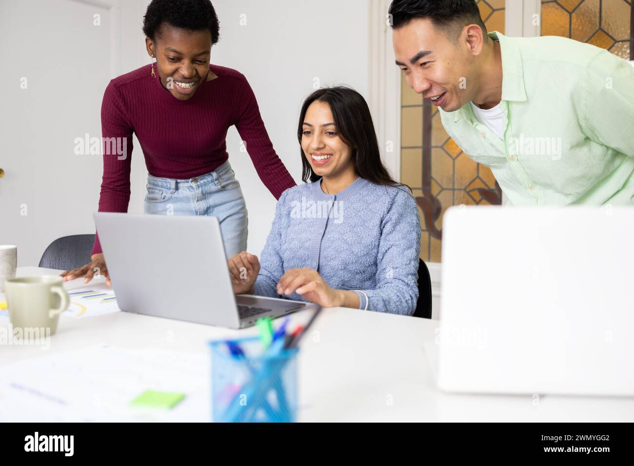 Drei Kollegen arbeiten mit einem Laptop in einer hellen Büroumgebung zusammen, tauschen Ideen aus und arbeiten an einem Projekt zusammen. Stockfoto