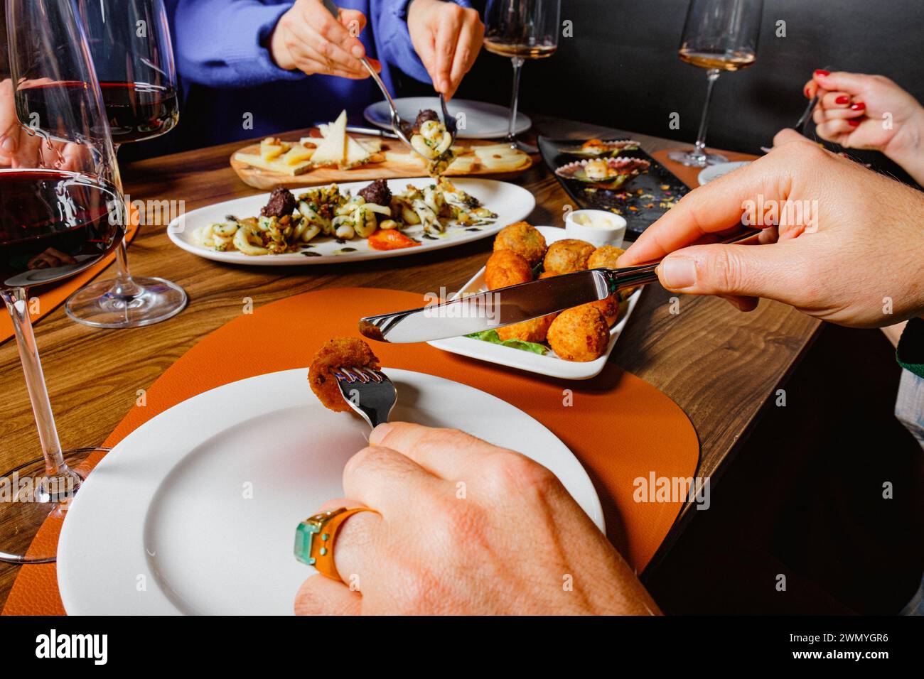 Gäste teilen sich eine Auswahl an Gourmetgerichten und Gläsern Rotwein an einem gemütlichen Esstisch Stockfoto
