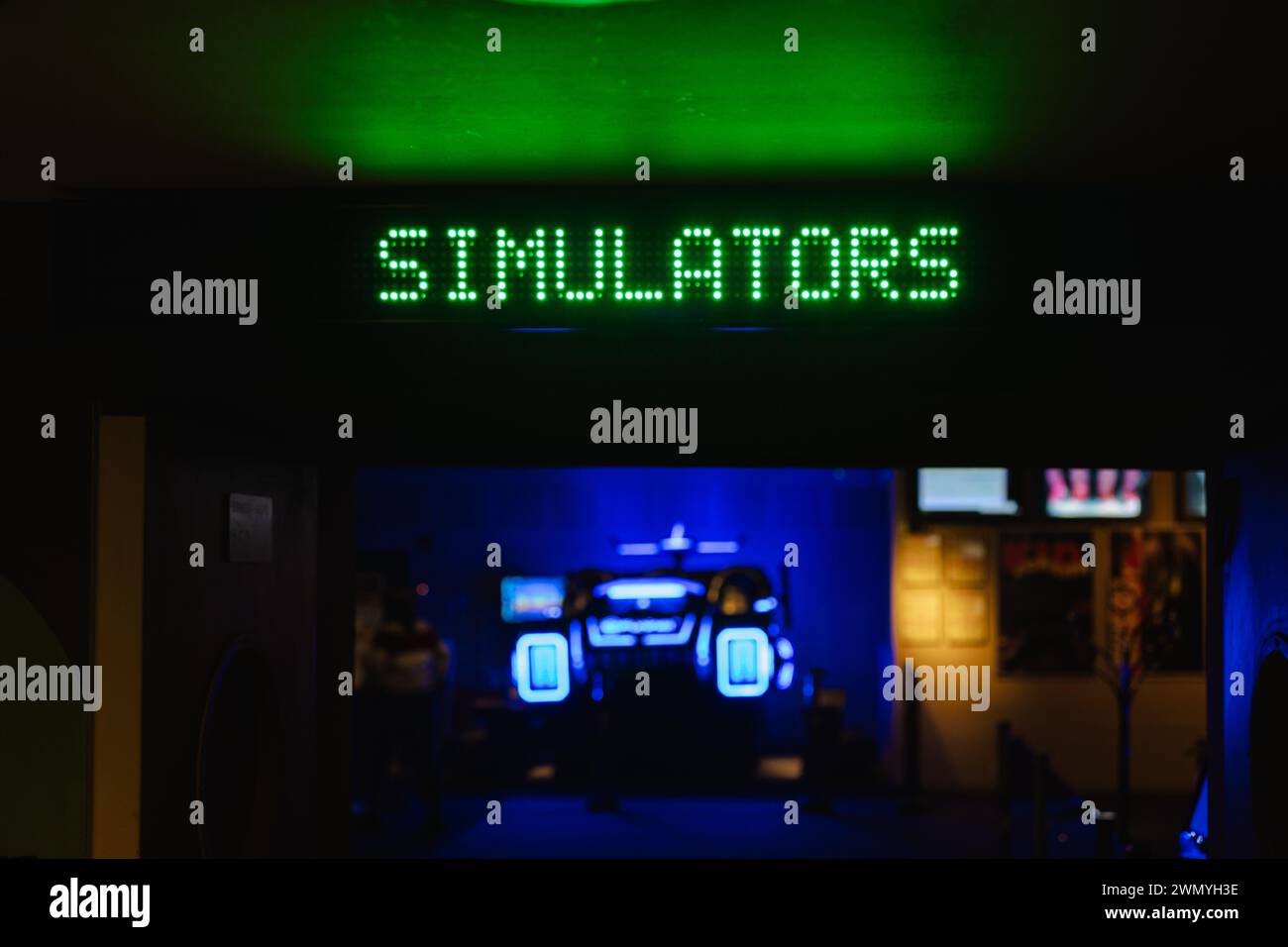 Grüne LED-SCHILDERSIMULATOREN in einem schwach beleuchteten Arkadenraum mit neonblauen Lichtern im Hintergrund Stockfoto