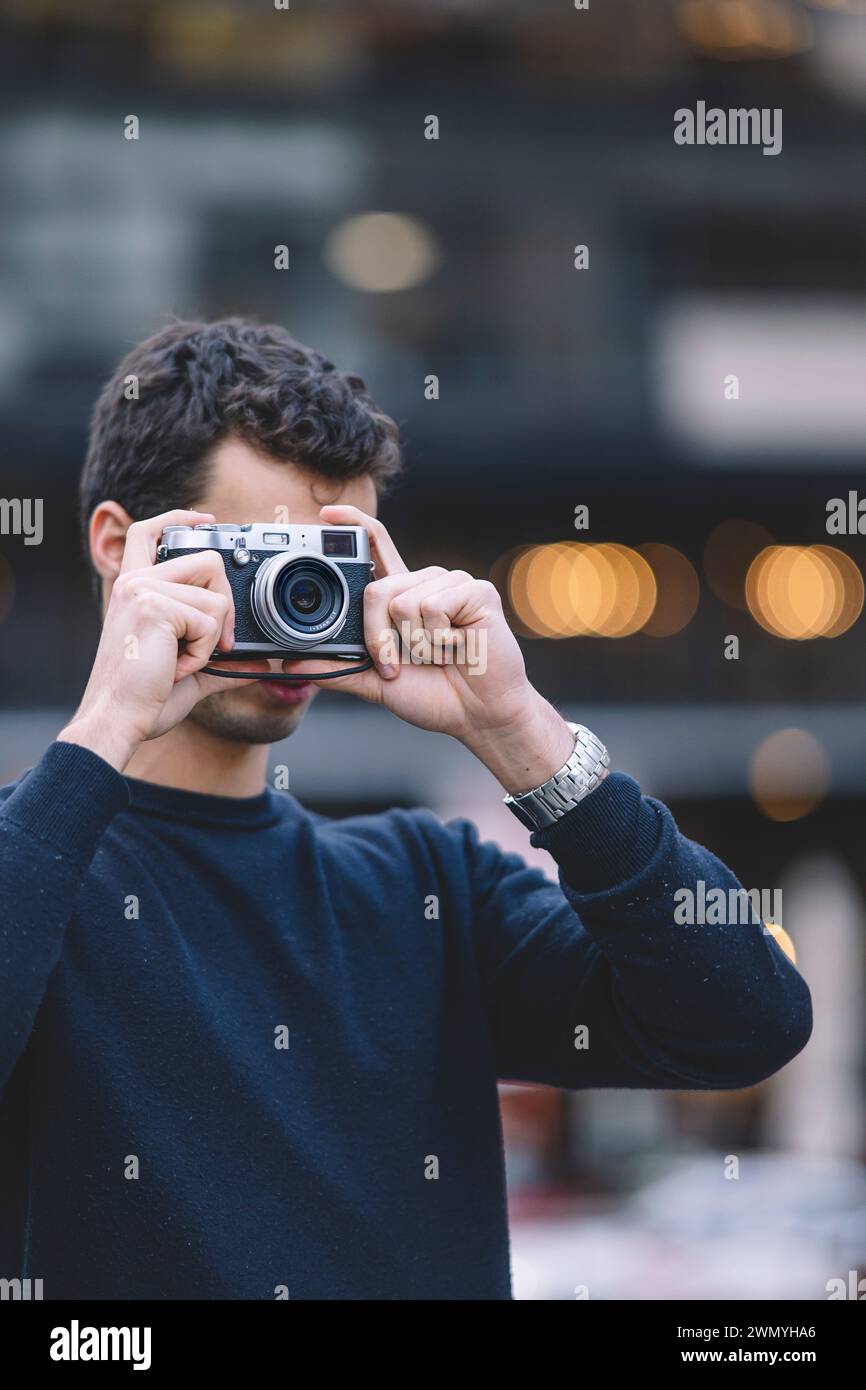 Junger Fotograf, der ein Foto mit einer Retro-Kamera aufnimmt, Bokeh-Lichter im Hintergrund Stockfoto