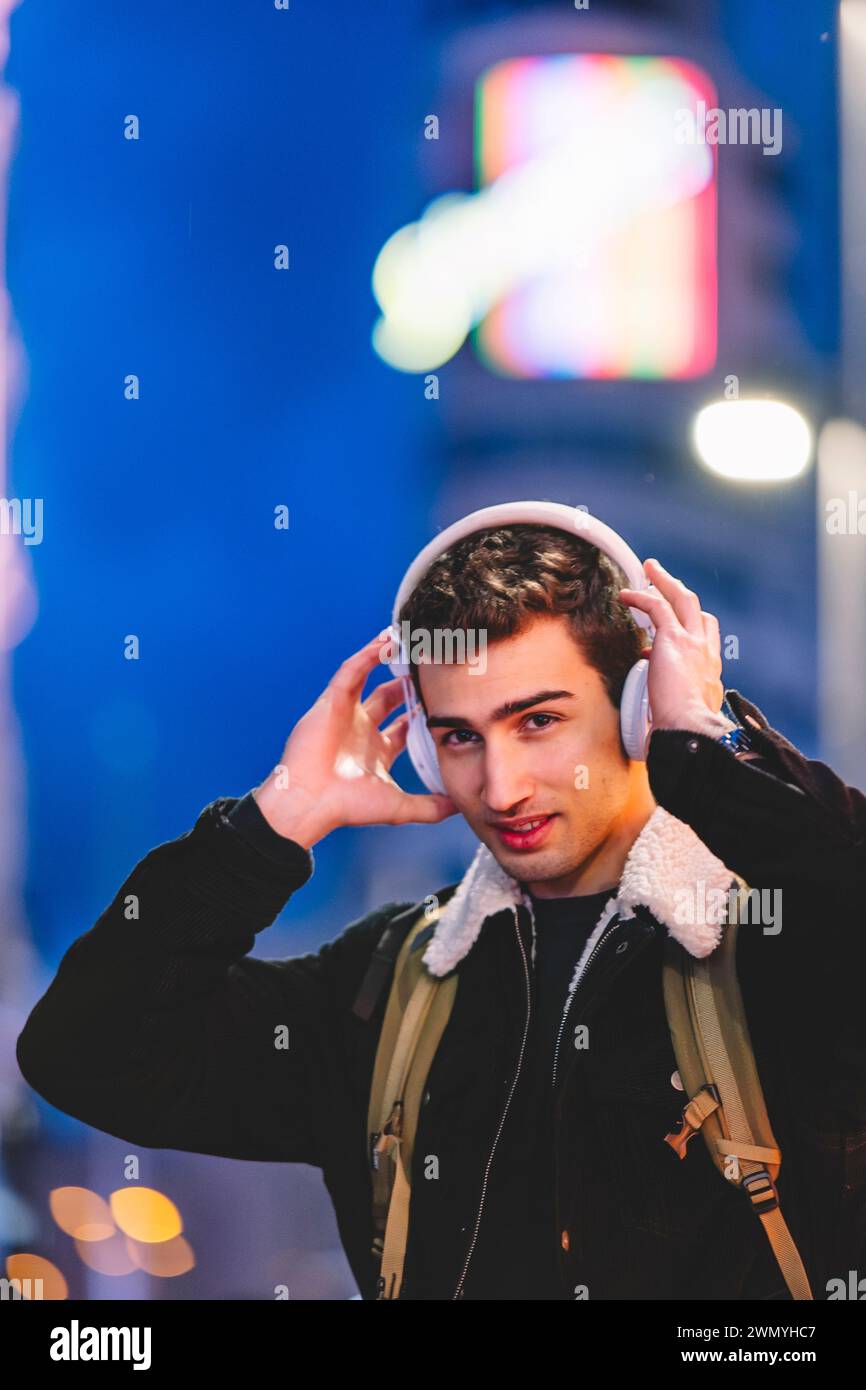Junger Mann mit Kopfhörern genießt nachts Musik in der Stadt, mit bunten Lichtern im Hintergrund Stockfoto