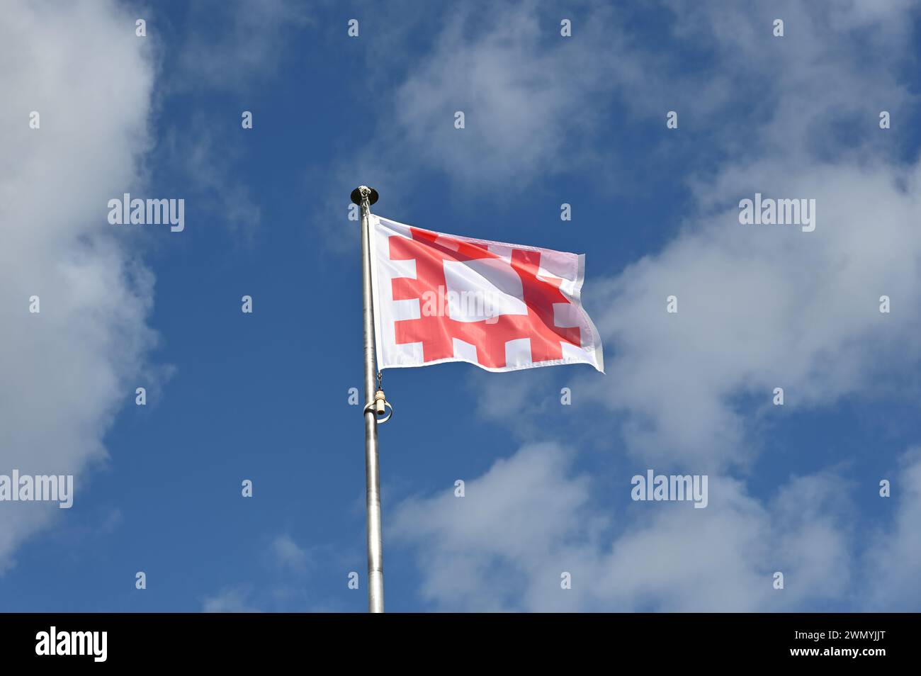 Die englische Heritage-Flagge fliegt gegen blauen Himmel und flauschige weiße Wolken Stockfoto