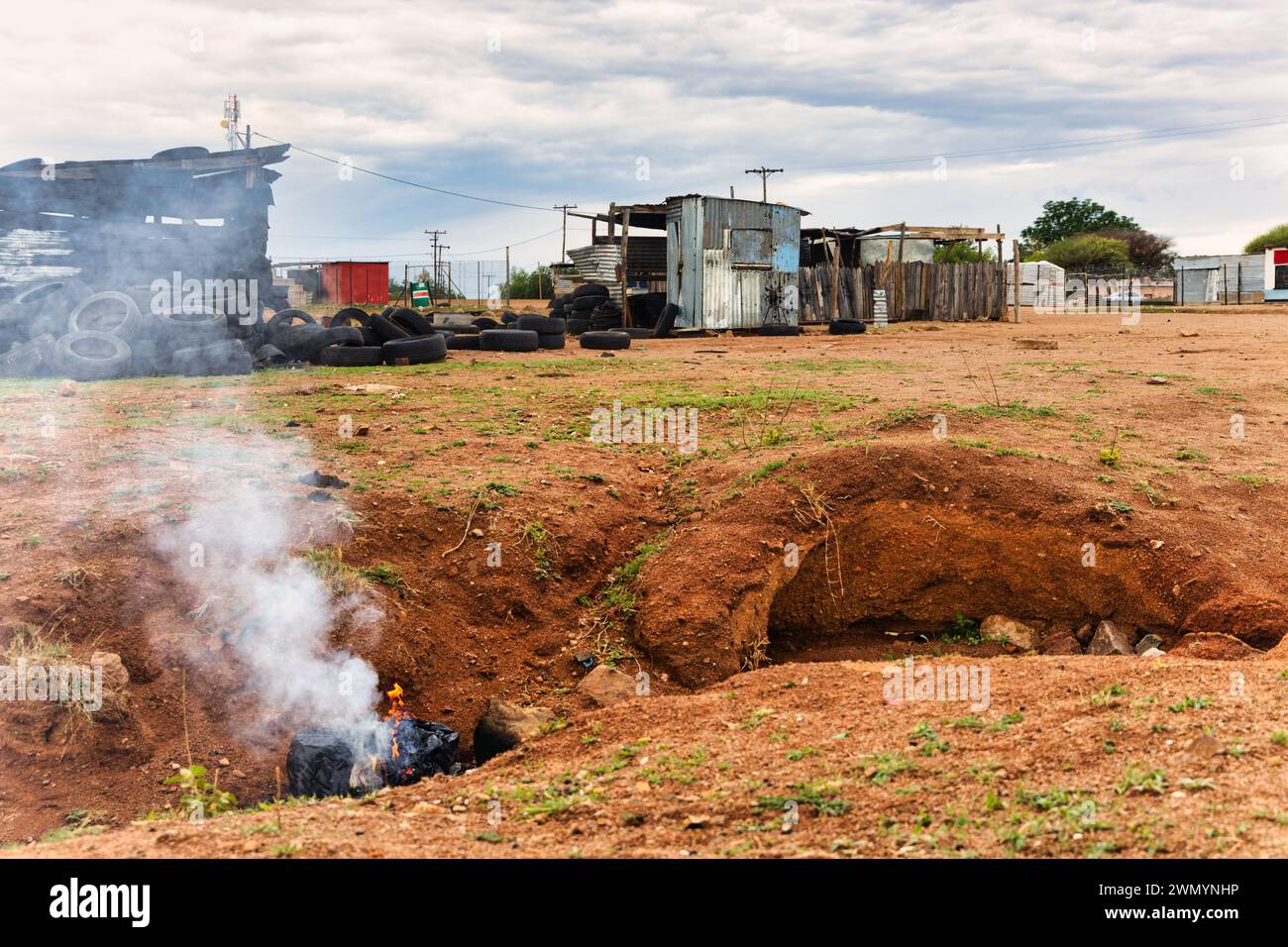 township informelle Siedlung in afrika in der Nähe eines Hügels, Hütte aus Wellblech und Holz, Müllsäcke brennen im Vordergrund Stockfoto