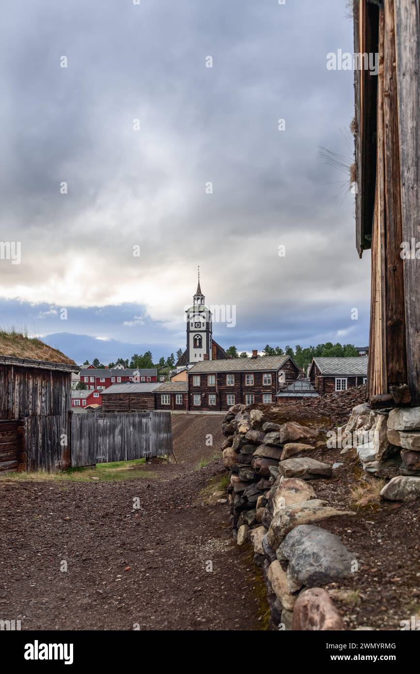 In dieser vertikalen Perspektive steht die Kirche Roros hoch zwischen den historischen Holzgebäuden, die von einem Pfad erfasst wurden. Norvay Stockfoto