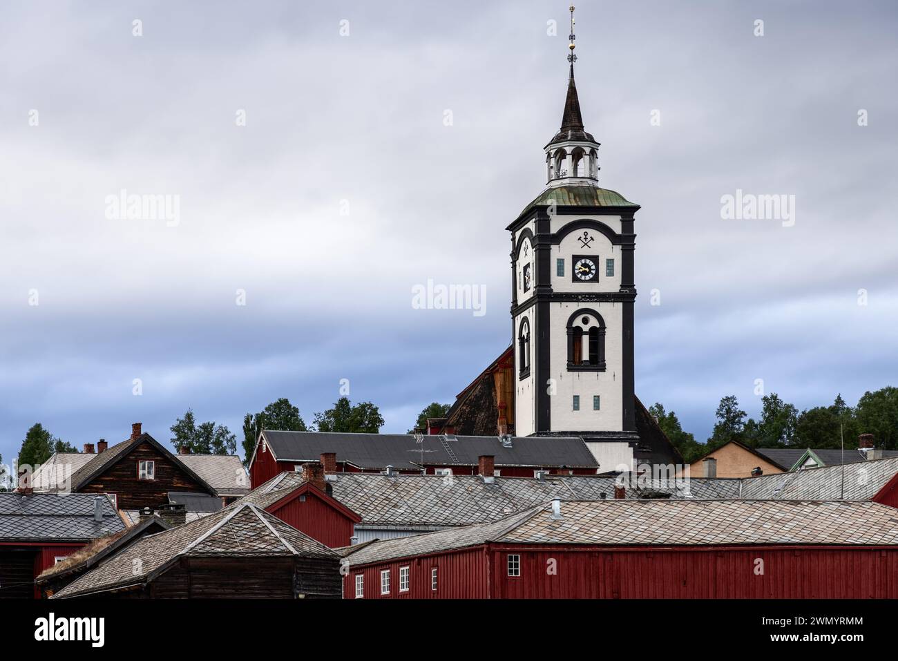 Die Kirche Roros steht inmitten traditioneller skandinavischer Holzhäuser unter einem bewölkten Himmel in diesem traditionsreichen nordischen Dorf Stockfoto