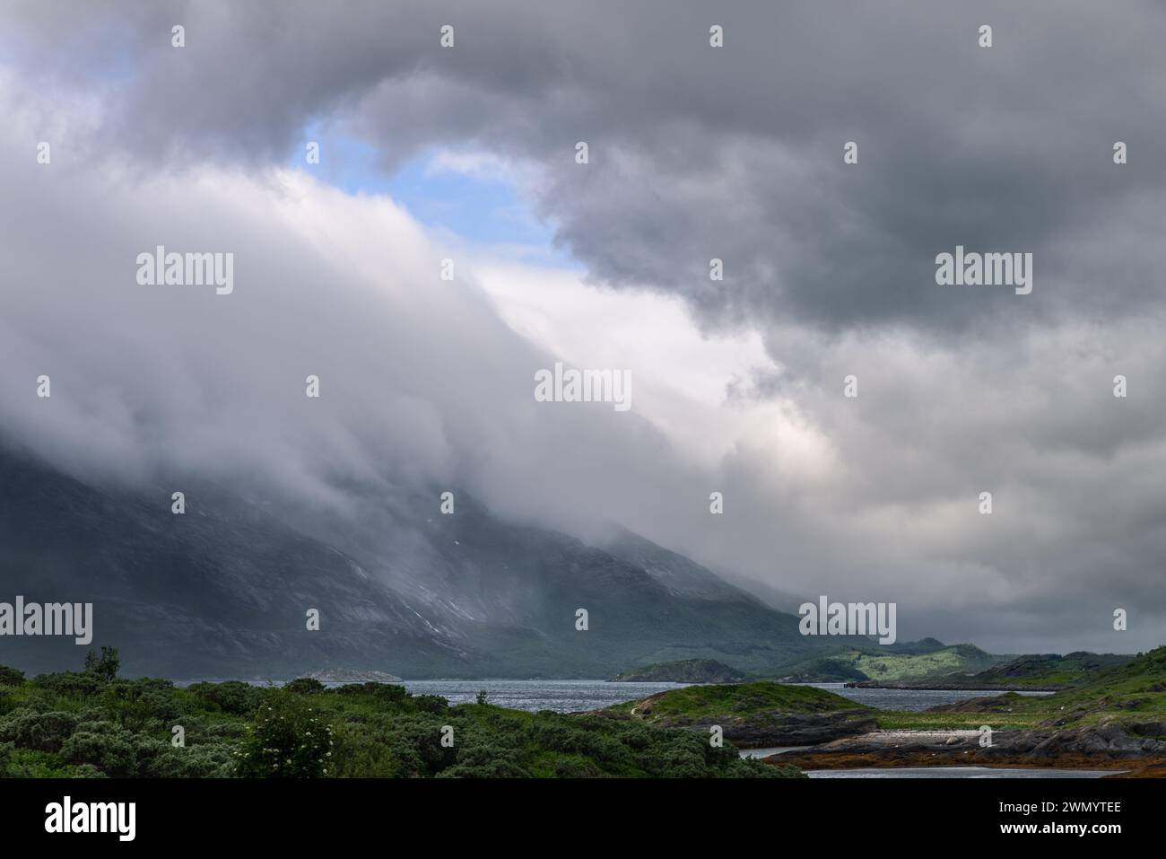 Ein dynamischer Sommerhimmel in Norwegen erstreckt sich über eine zerklüftete Landschaft, in der Berge und Laub in der Nähe des Polarkreises von rollendem Nebel gestreichelt werden Stockfoto