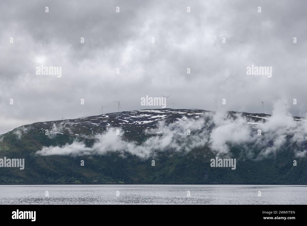 Windturbinen erheben sich auf einem norwegischen Berg über den Horizont, ihre Rotorblätter schneiden durch den Nebel und stellen erneuerbare Energien der zeitlosen Wildnis gegenüber Stockfoto