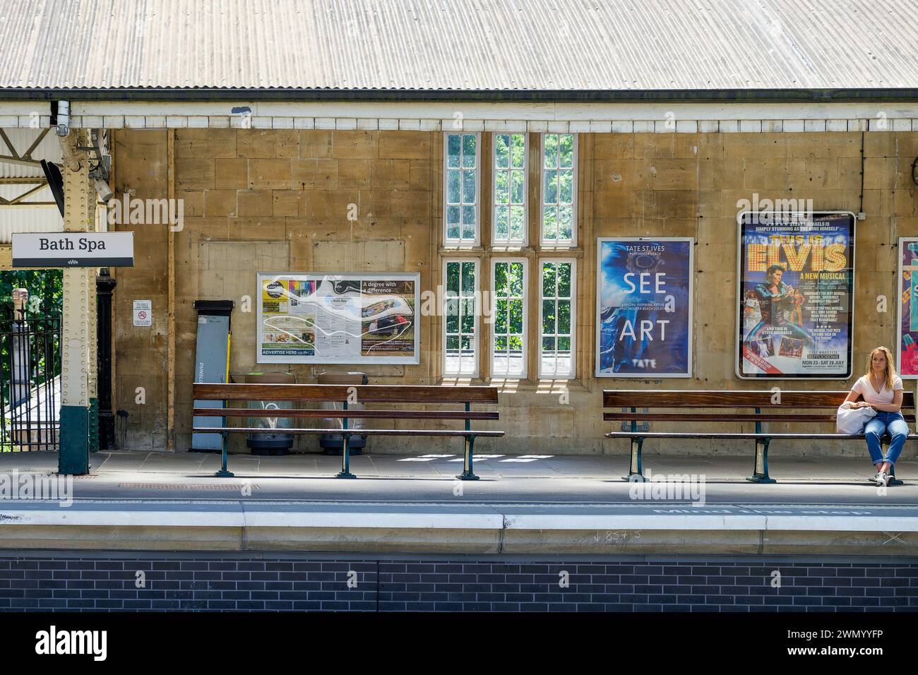 Eine Frau ist auf einem Bahnsteig abgebildet, der auf einem Sitz sitzt und auf einen Zug wartet. Stockfoto