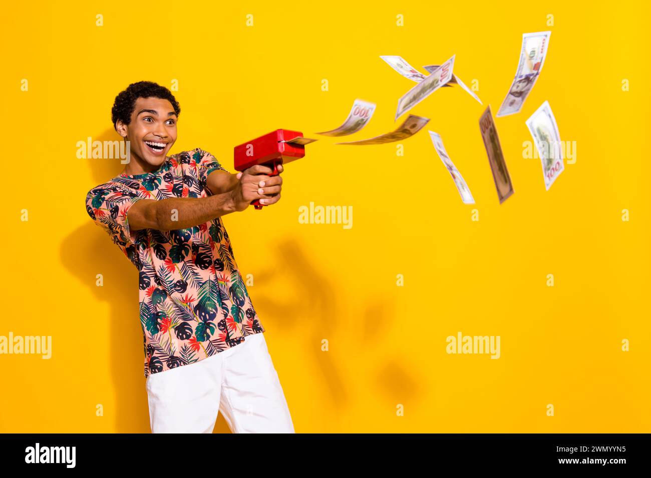 Foto eines jungen, überglückten Millionärs, reichen Mannes im Casino, der sein Gehalt mit einer Maschinenpistole auf gelbem Hintergrund schießt Stockfoto