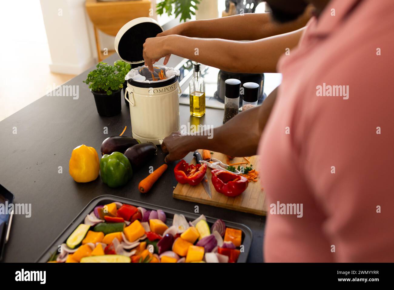 Ein Afroamerikaner fügt Essensreste in einen Kompostbehälter in einer Küche zu Hause Stockfoto