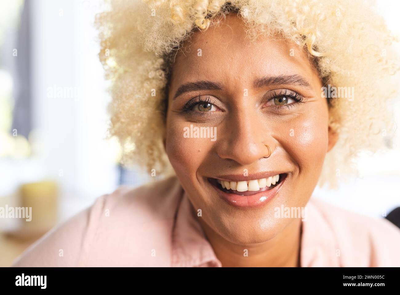 Eine junge Frau mit lockigen blonden Haaren lächelt warm und trägt ein hellrosa Hemd Stockfoto