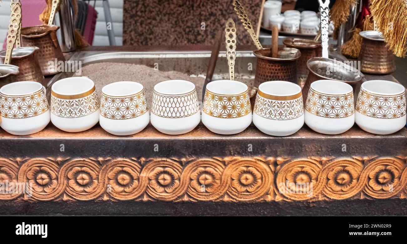 Heiße Kaffeemaschine im Sand. Kaffeetassen auf dem Display des Coffee-Shops. türkischer Kaffee zubereiten. Straßenfoto, niemand Stockfoto