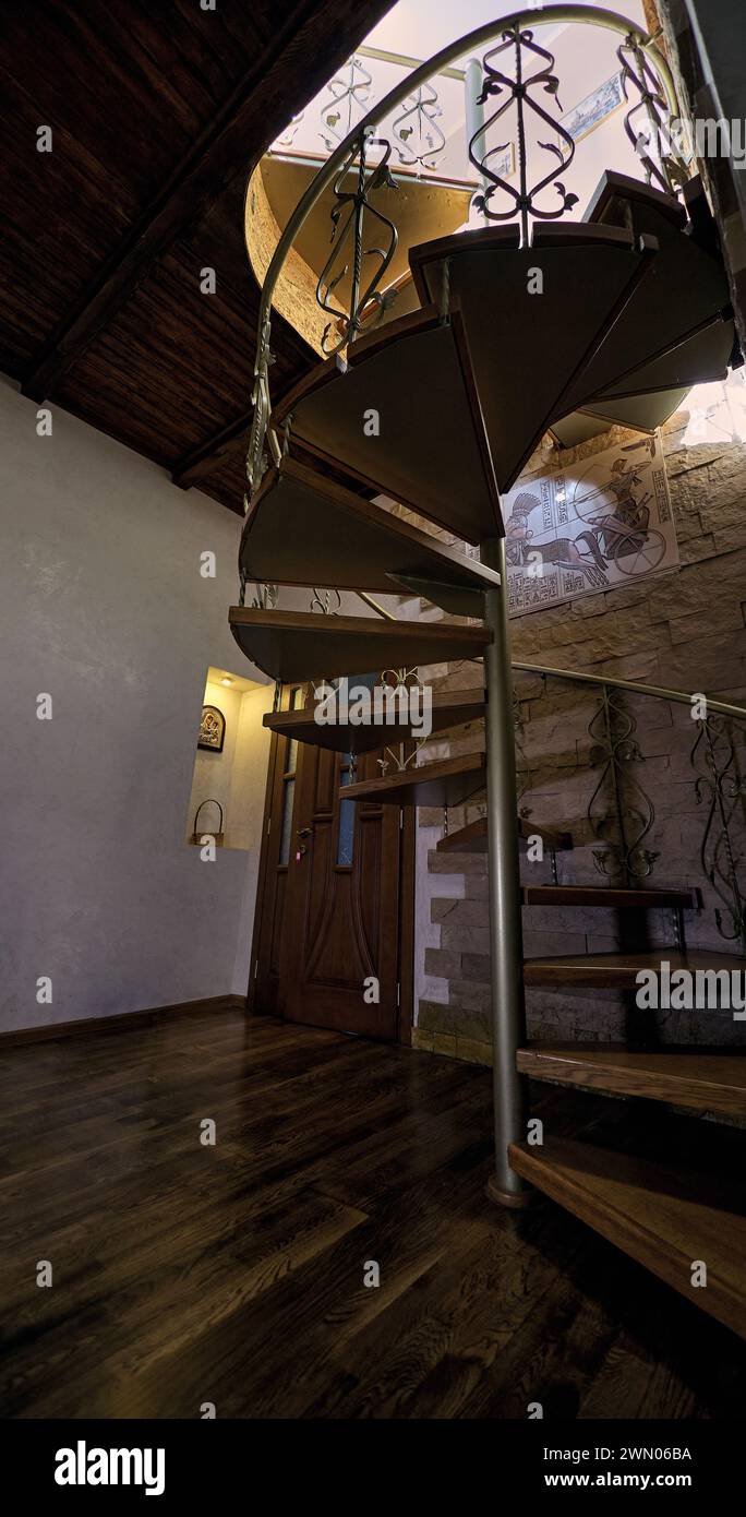 Innenraum-Wendeltreppe aus Metall mit Holztreppen und dekorativen Metallgeländern. Mit Holztür auf Hintergrund Stockfoto