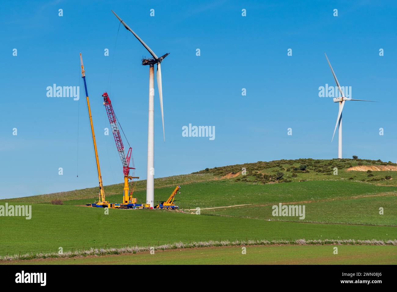 Riesige Kräne neben einer Windturbine, die einen Brand erlitten hat, Hochhubkrane, um die beschädigte Turbine und Propeller auszutauschen. Stockfoto