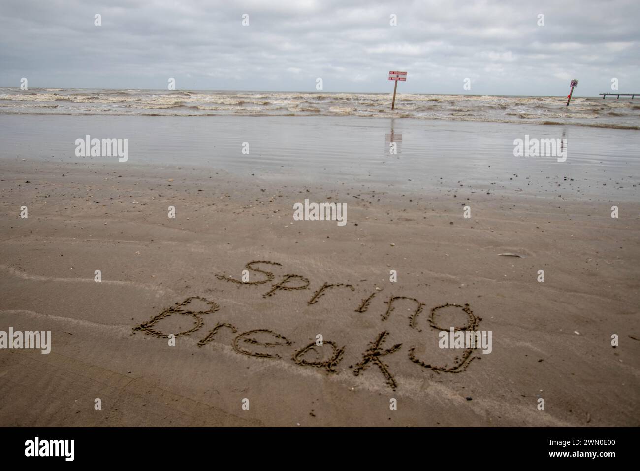Schreiben im Sand an der Küste des Golfs von Mexiko. Kurven im Hintergrund mit Warnzeichen. Ein teilweise bewölkter Tag am Strand in Galveston TX. Stockfoto