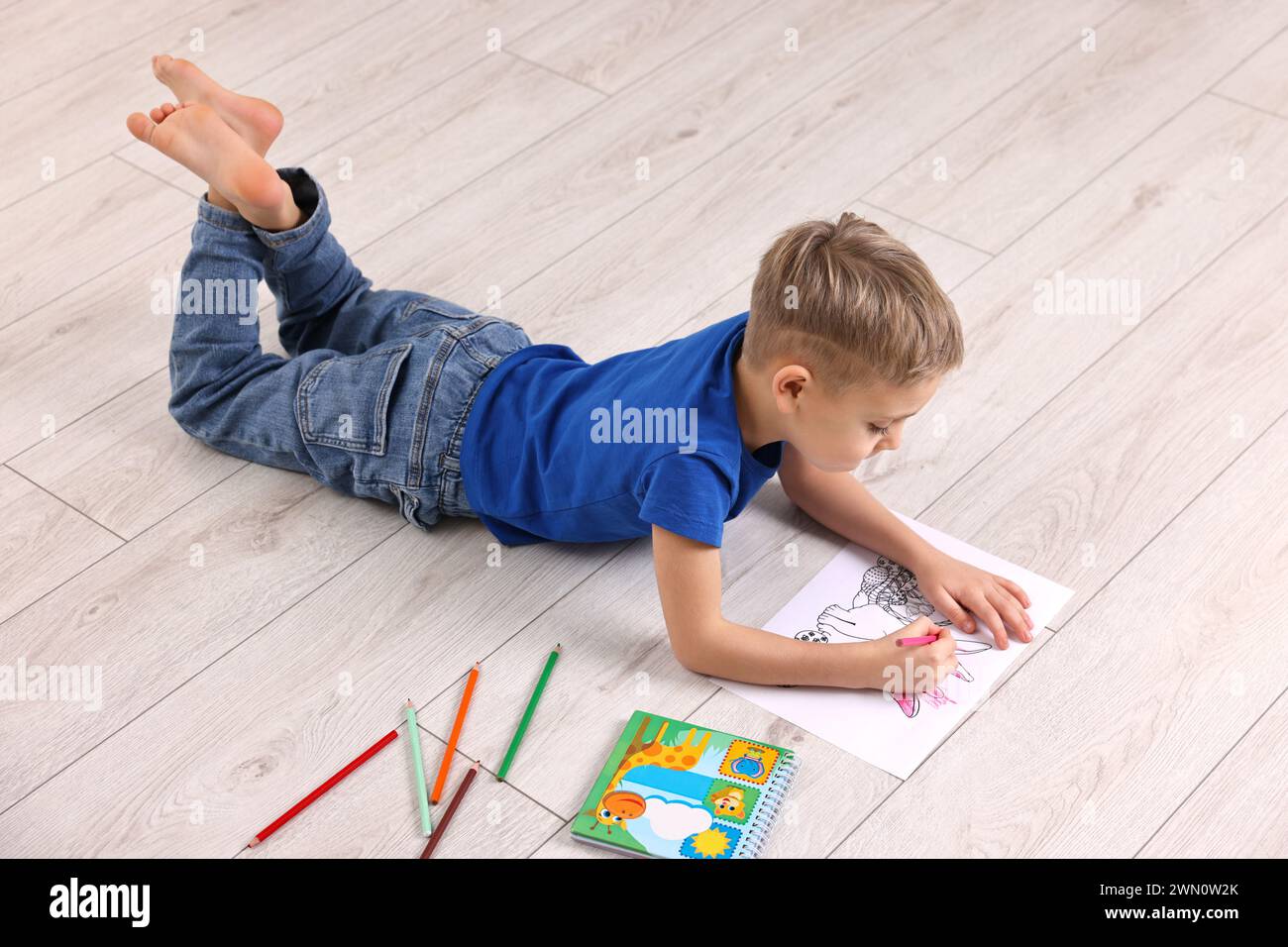 Niedlicher kleiner Junge, der zu Hause auf dem warmen Boden zeichnet. Heizung Stockfoto