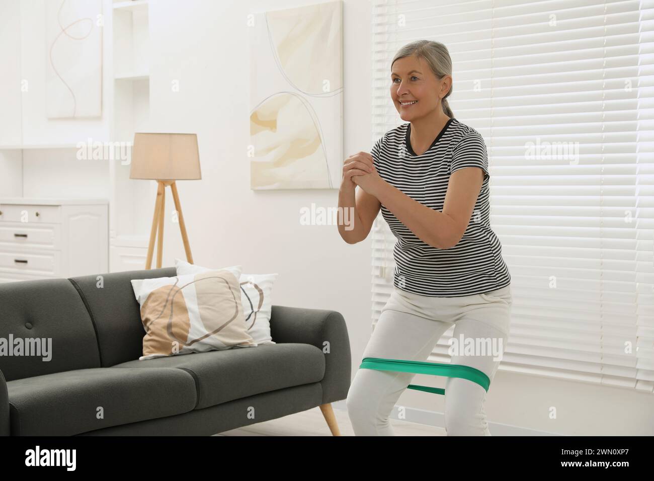 Ältere Frau, die zu Hause Squats mit elastischem Fitnessband macht Stockfoto