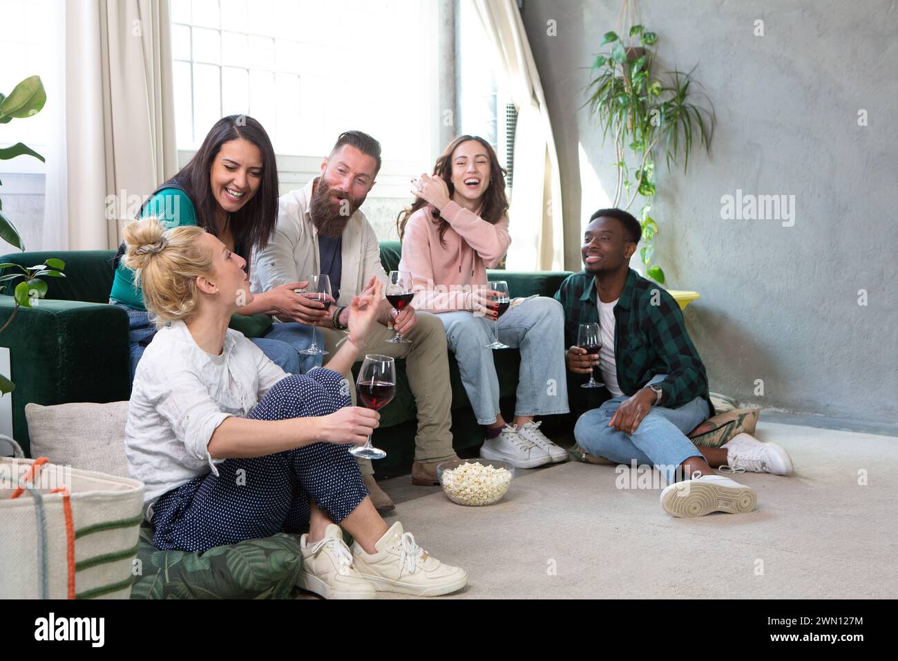 Freunde, die in einem gemütlichen Wohnzimmer sitzen, unterhalten sich bei einem Glas Wein in entspannter Atmosphäre, umgeben von heimischem Komfort Stockfoto