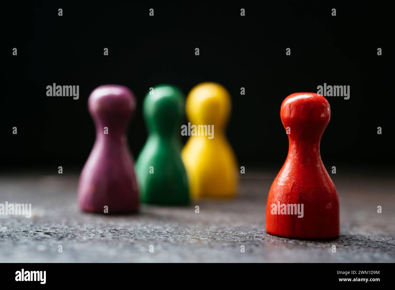 Drei Spielfiguren im Stil eines Bauern stehen zusammen und ein rotes in einer Entfernung von ihnen. Stockfoto