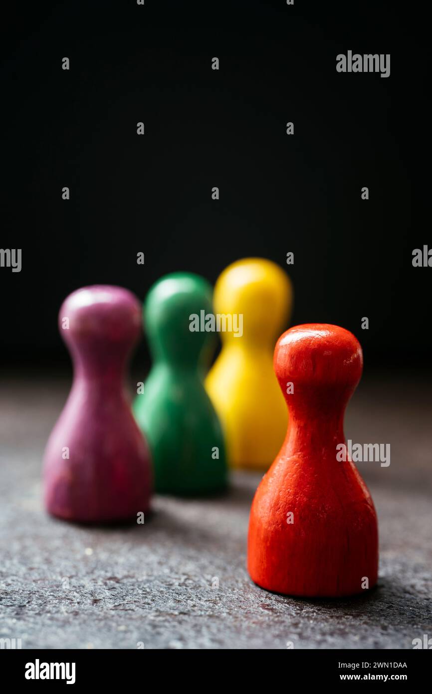 Drei Spielfiguren im Stil eines Bauern stehen zusammen und ein rotes in einer Entfernung von ihnen. Stockfoto