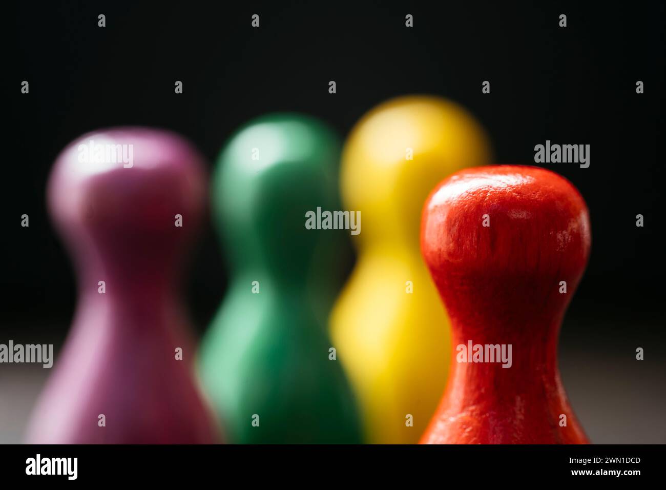 Drei Spielfiguren im Stil eines Bauern stehen zusammen und ein rotes in einer Entfernung von ihnen. Stockfoto