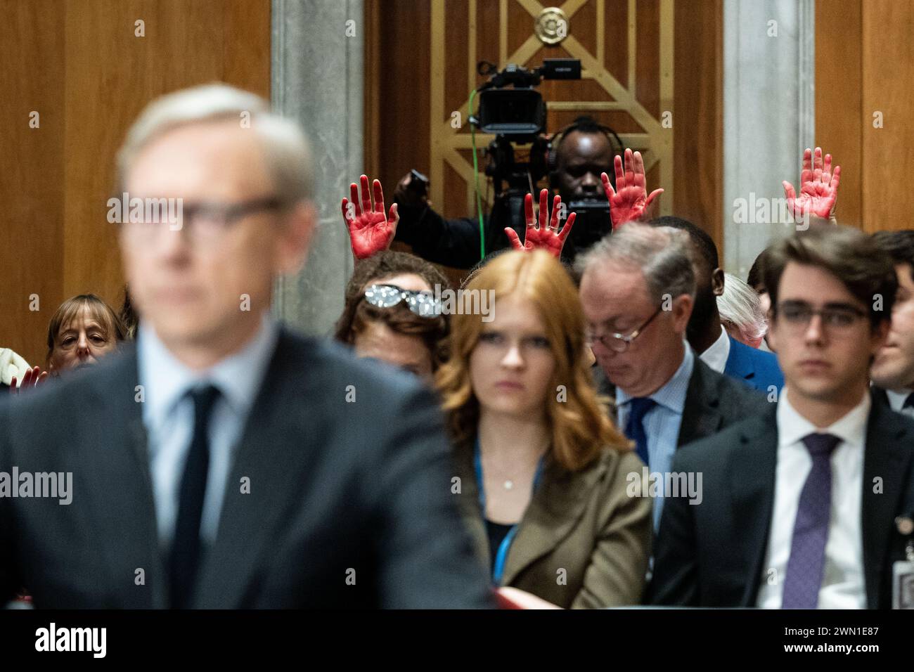 Washington, Usa. Februar 2024. Aktivisten mit roten Händen (mit Brian Hook, Vice Chairman, Cerberus Global Investments, LLC, Cerberus Capital Management auf der linken Seite) hielten sich bei einer Anhörung des Senat Foreign Relations Committee im US Capitol. Quelle: SOPA Images Limited/Alamy Live News Stockfoto