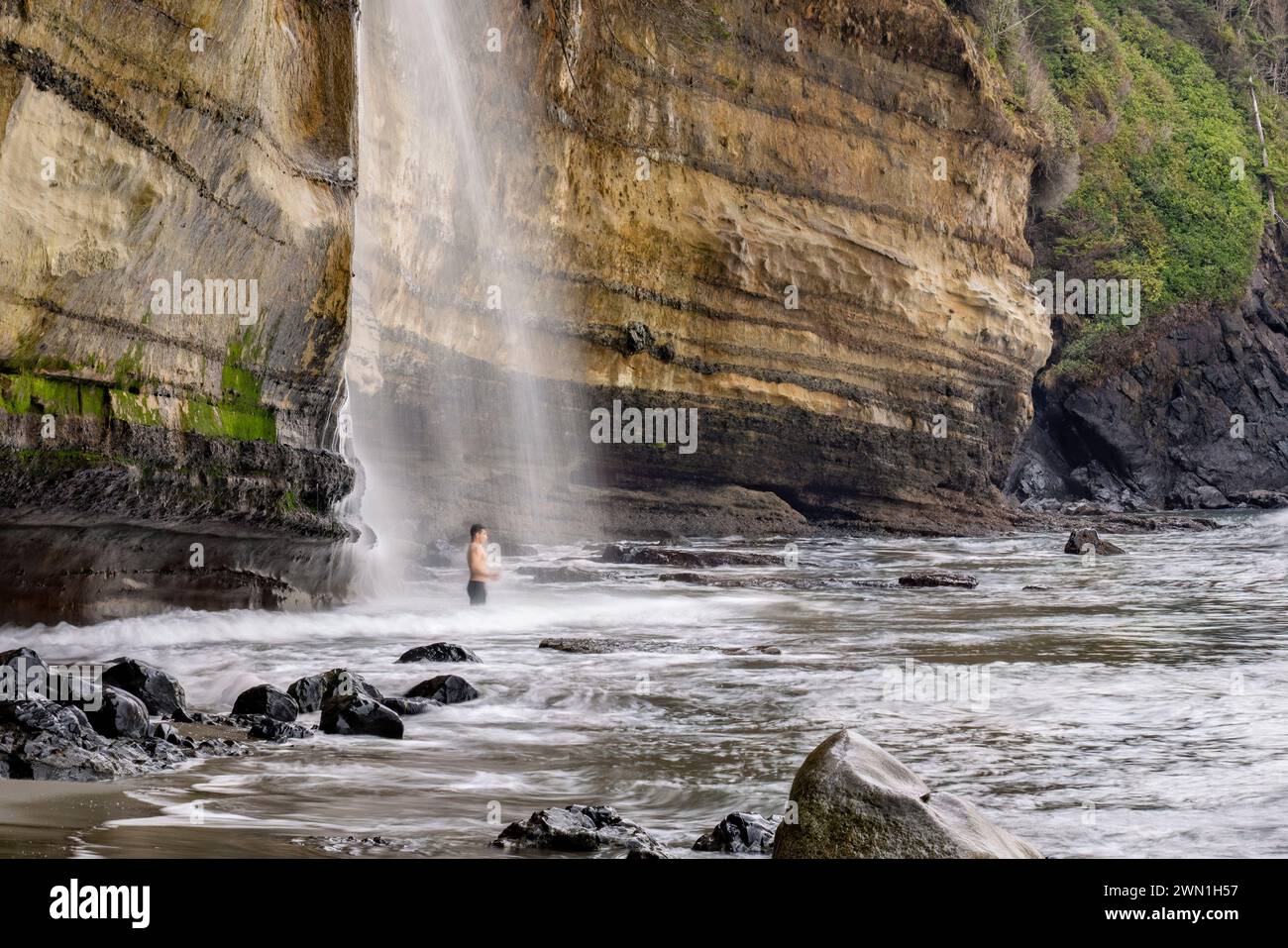 Person, die im kalten Wasser der Mystic Beach Falls steht - in der Nähe von Sooke, Vancouver Island, British Columbia, Kanada Stockfoto