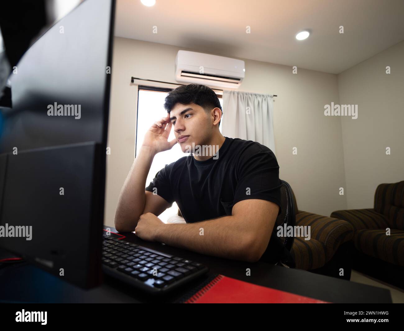 Ein junger Mann zeigt Müdigkeit, Entmutigung und Frustration vor seinem Computer und bewältigt die Herausforderungen, von zu Hause aus zu arbeiten und zu studieren Stockfoto