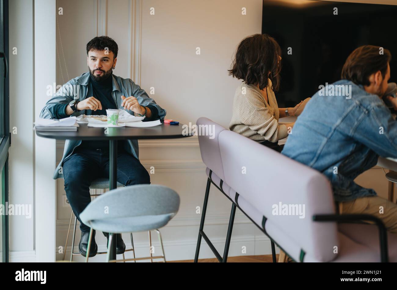 Drei Profis nehmen an einem zwanglosen Business Lunch Meeting in einem modernen Bürobereich Teil und genießen eine Mahlzeit. Stockfoto