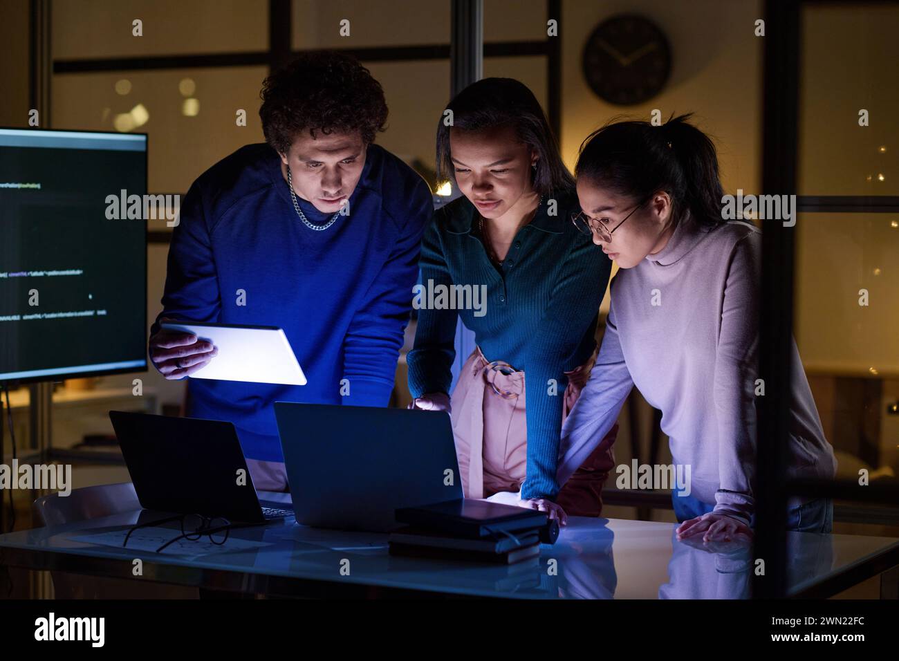 Drei ethnisch unterschiedliche Programmierer arbeiten nachts im Büro des IT-Unternehmens an neuer Software Stockfoto