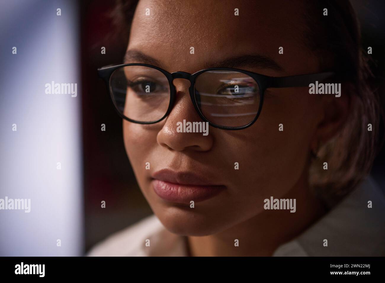 Nahaufnahme einer jungen Programmiererin, die eine Brille trägt und spät nachts im Büro des IT-Unternehmens an Code arbeitet Stockfoto