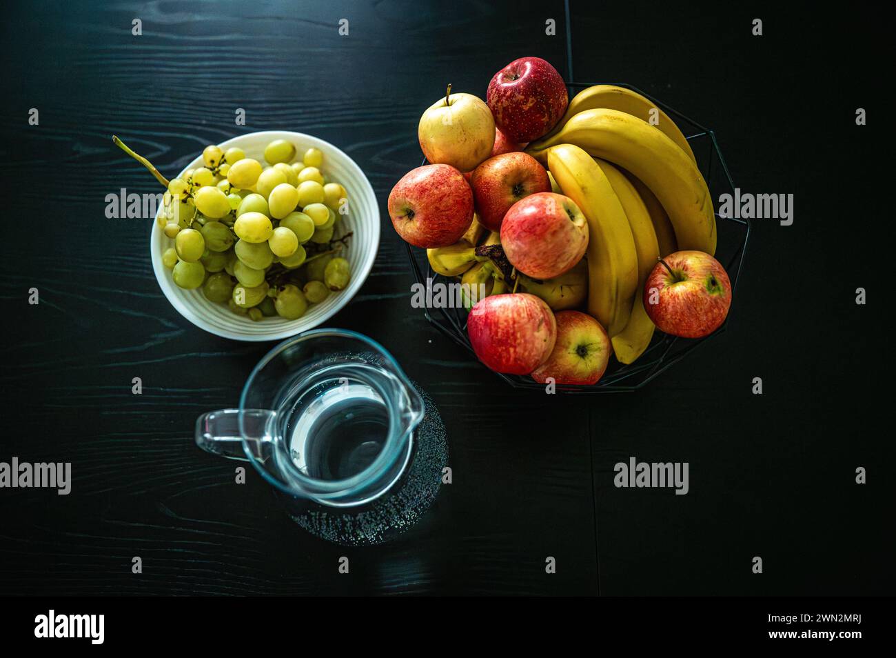 Banane, Apfel und Trauben auf einem dunklen Küchentisch Stockfoto