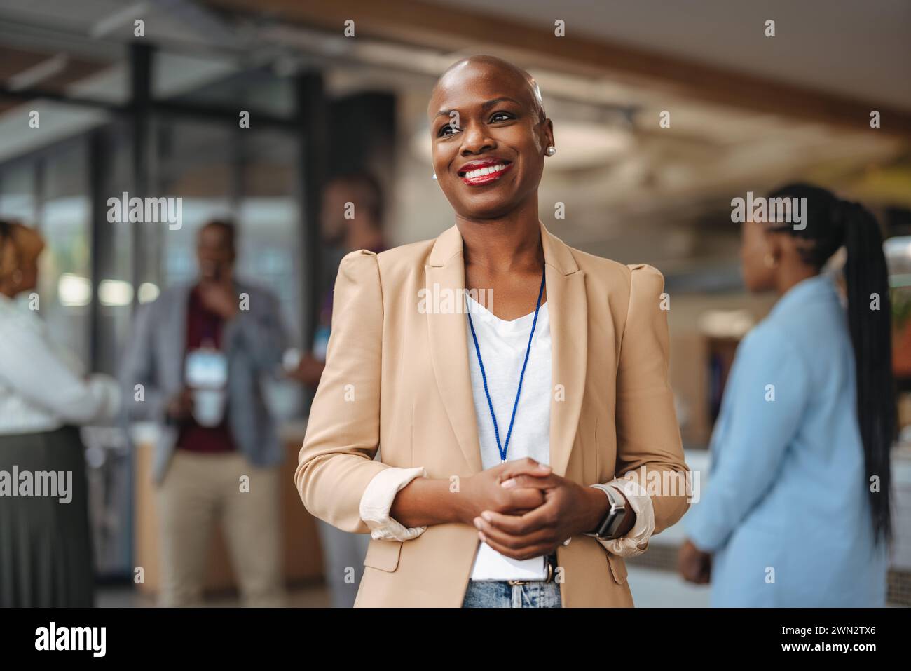 Professionelle Geschäftsfrau mit strahlendem Lächeln steht selbstbewusst in einem modernen Büroumfeld und reflektiert Positivität und Führungsstärke wie ihre Kollegen Stockfoto