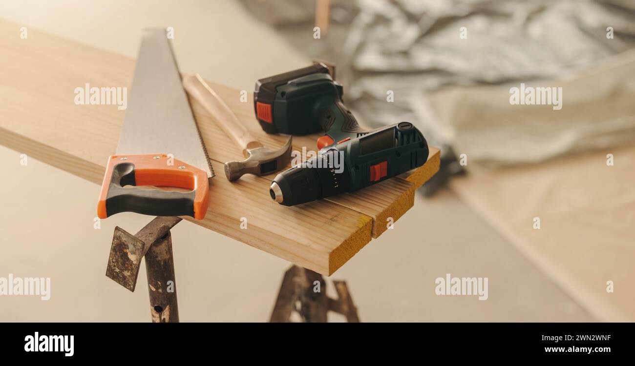 Werkzeuge und Ausrüstung für ein Heimwerkerwohnungsprojekt. Eine Stillleben-Szene mit Hammer, Bohrmaschine und Quersäge sowie Holz und Basis Stockfoto