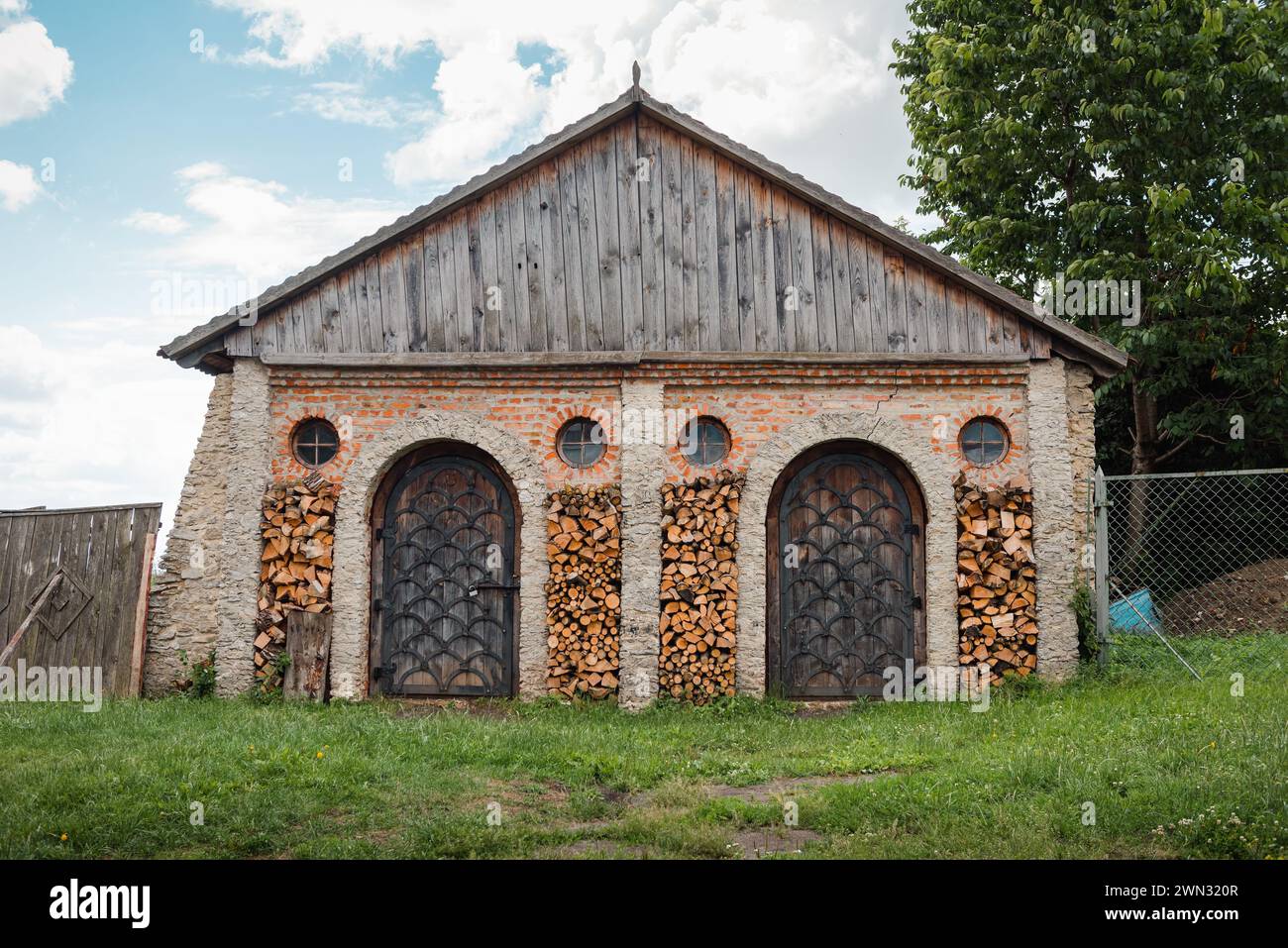 Schmiede der Burg Dubno aus dem 15. Jahrhundert mit Holzstapeln, die Aussparungen der Fassade füllen. schmiedegebäude mit Holztüren und runden Fenstern. Stockfoto