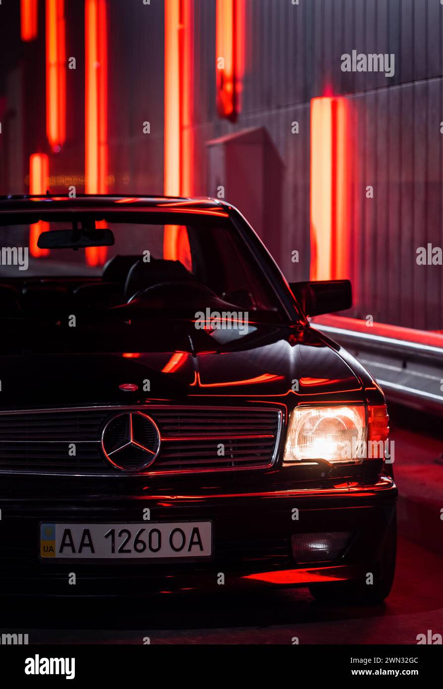 Schwarzes Mercedes Benz SEC Coupé bei Nacht in der Nähe der Neonwand. Frontansicht eines Mercedes der 1980er Jahre mit eingeschalteten Scheinwerfern Stockfoto