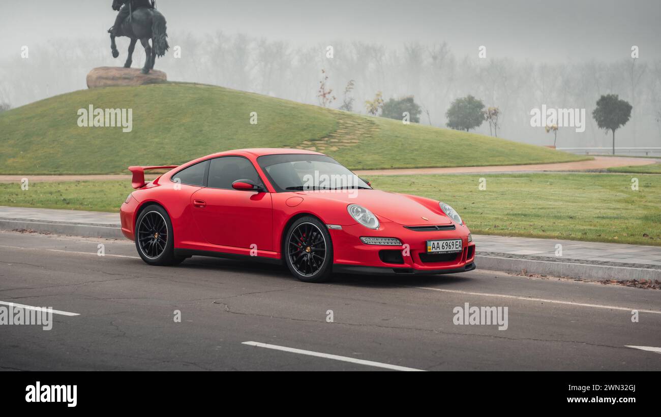 Roter Porsche 911 an einem nebeligen Morgen. Dreiviertelansicht des Sportwagens Porsche 997 vor dem Pferdedenkmal auf einem Hügel. Stockfoto