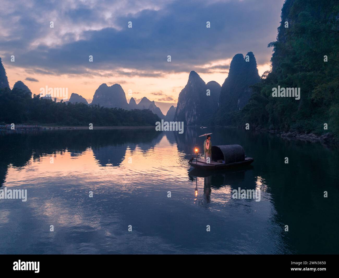 Ein Tourist in chinesischer Tracht macht bei Sonnenaufgang Fotos auf dem Fluss Li Stockfoto